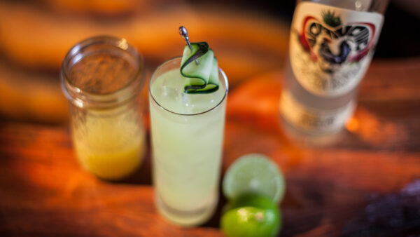 Mixed drink on a bar with freshly cut lime. Cup of juice to the left of the glass and a bottle of liqure to the right.